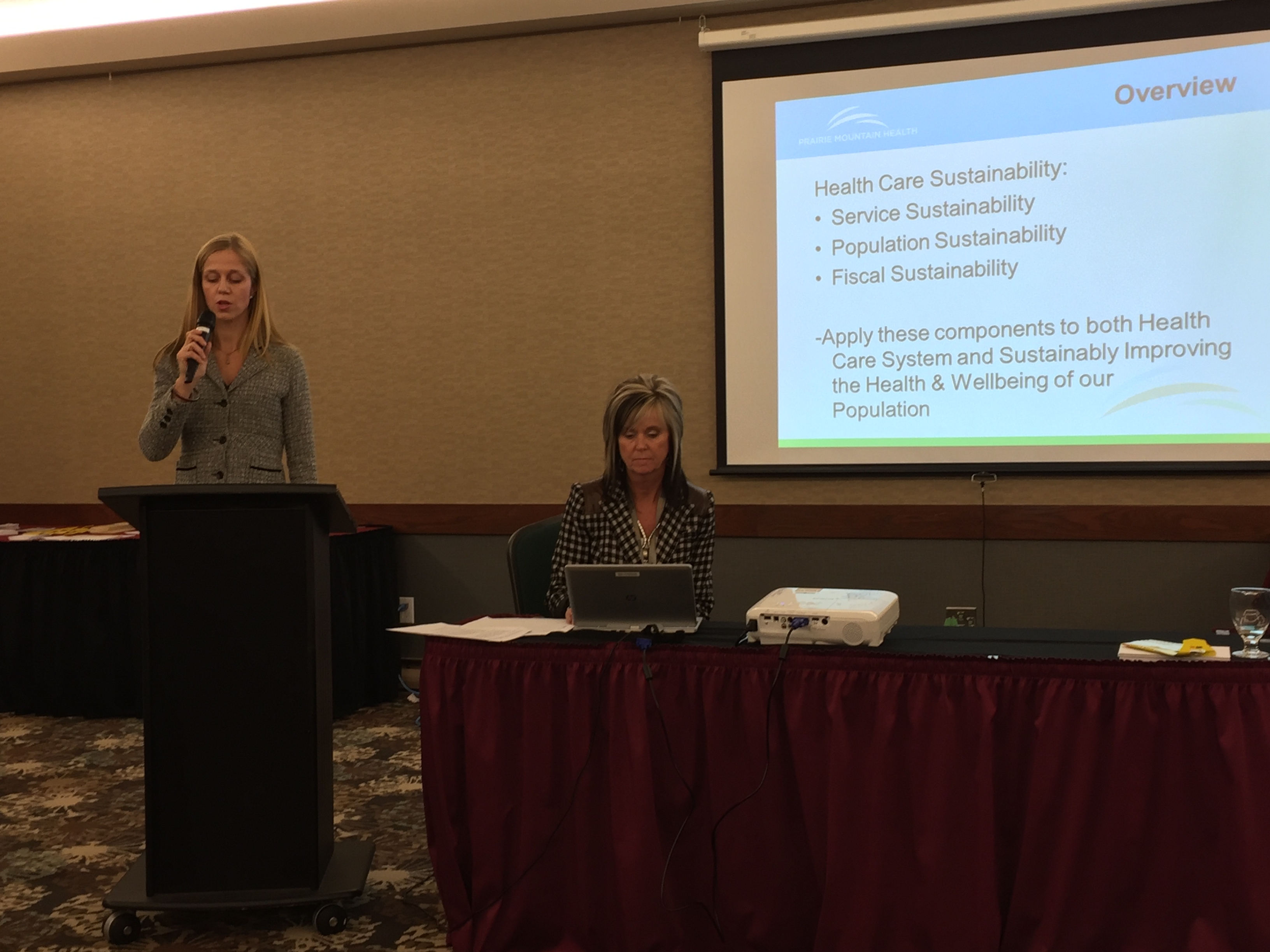 Dr. Amy Frykoda speaking at PMH AGM with CEO Penny Gilson at the computer